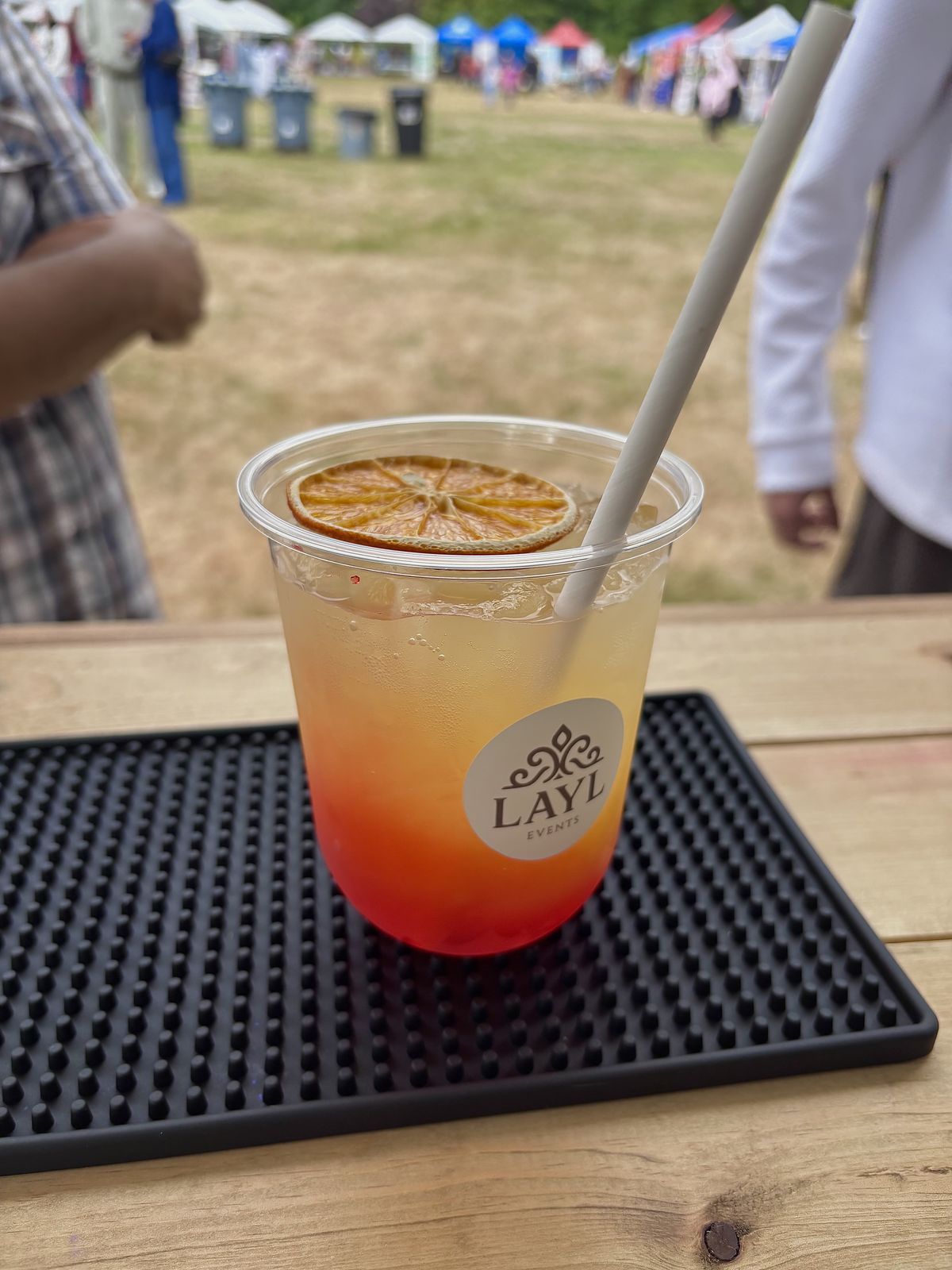 A Golden Hour mocktail with a dried orange slice at a busy outdoor community festival